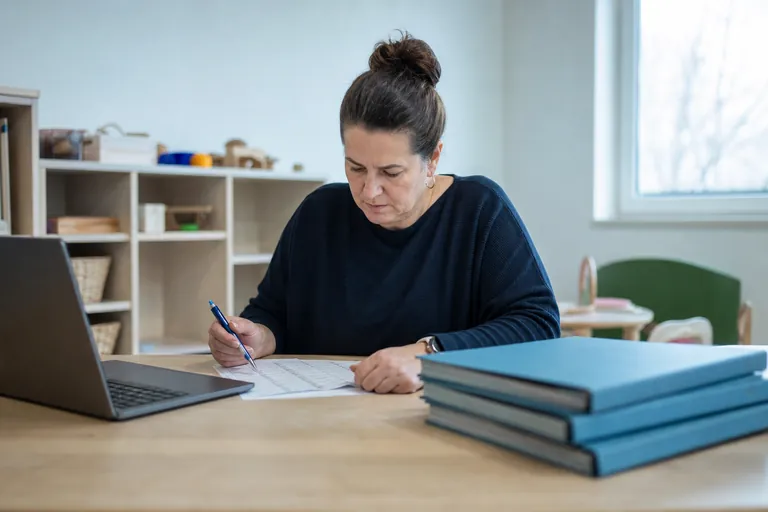Eine Kita-Leitung prüft mit einer Checkliste Kinderakten und digitale Unterlagen.