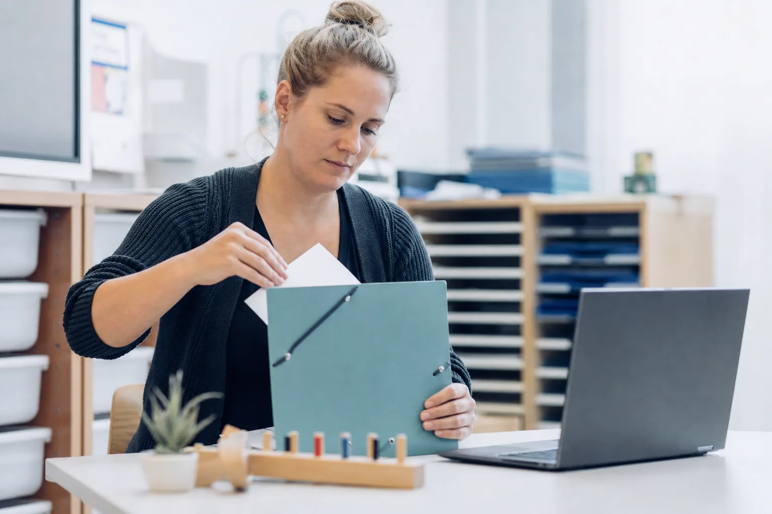 Eine Fachkraft sortiert einen Nachweis in eine Kinderakte und dokumentiert den Vorgang am Laptop.